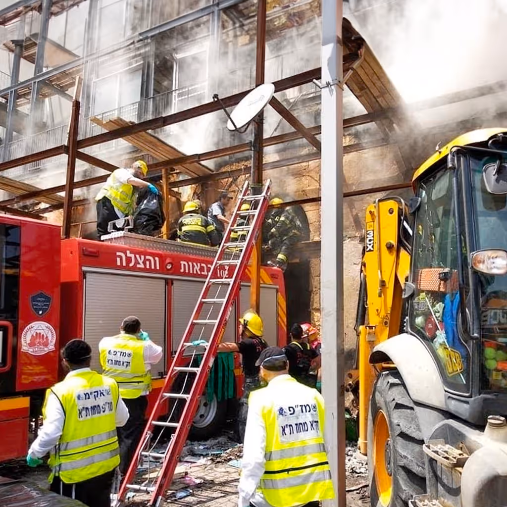 Emergency responders in yellow vests and helmets near a red fire truck using a ladder on a smoky building under construction.