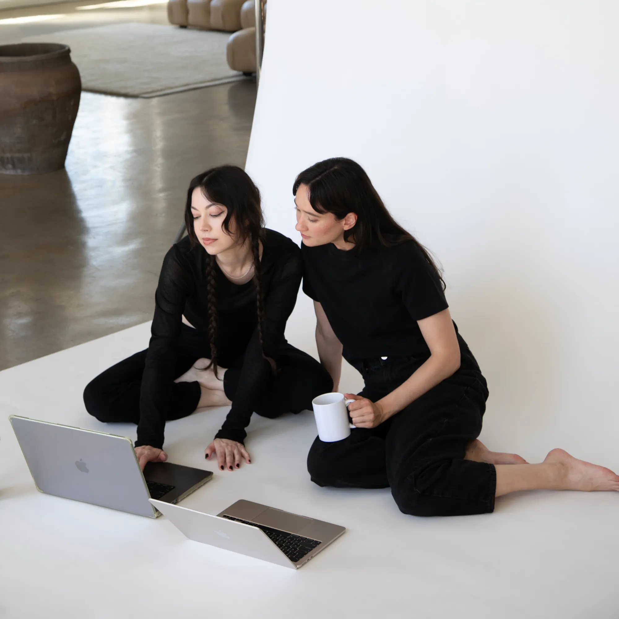 Two women sitting on the floor looking at a laptop.