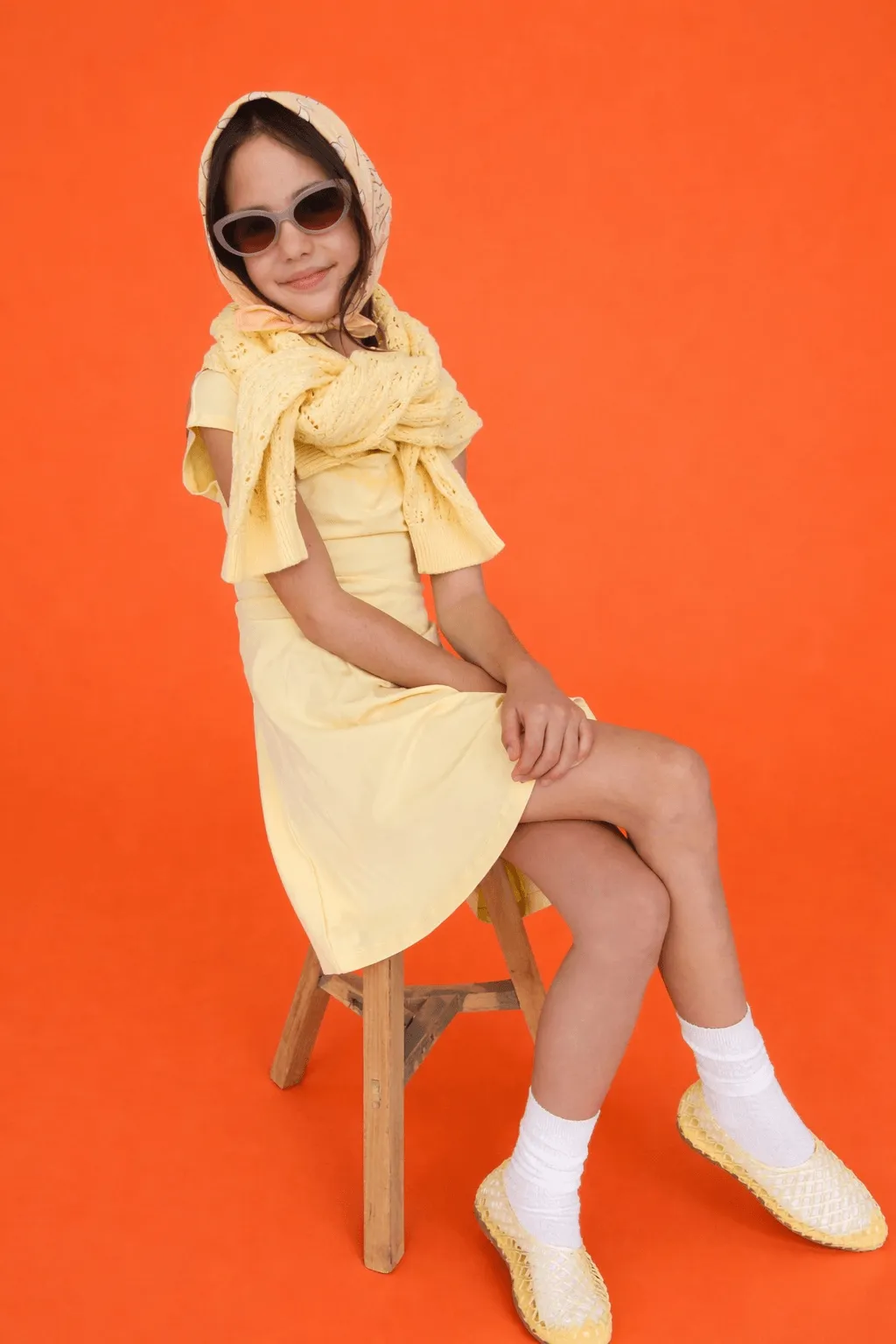 A little girl in a yellow dress sitting on a chair.