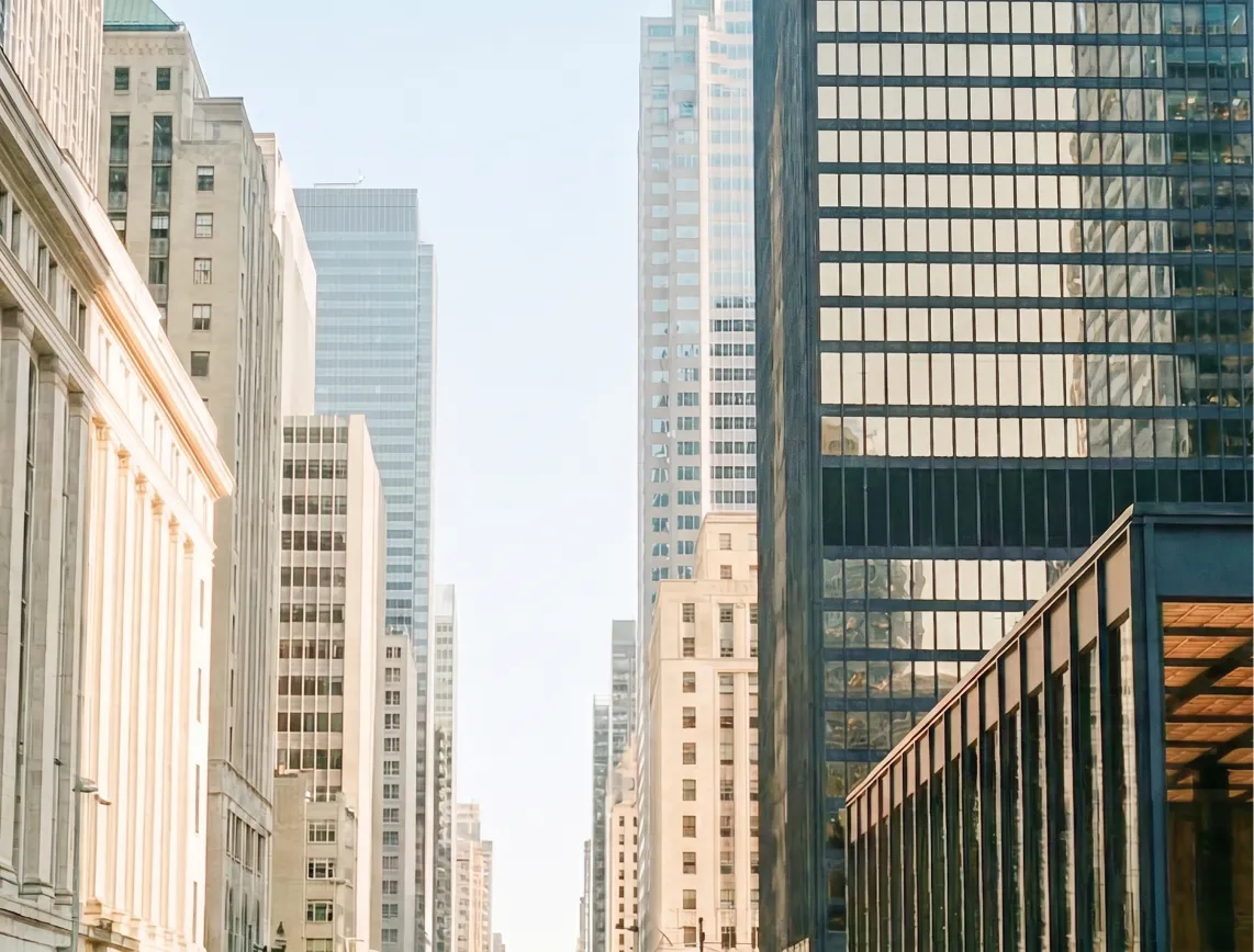 View of a city street lined with tall modern and classic office buildings under a clear sky.