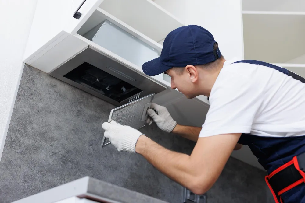`Technician removing a range hood grease filter during a kitchen appliance repair`