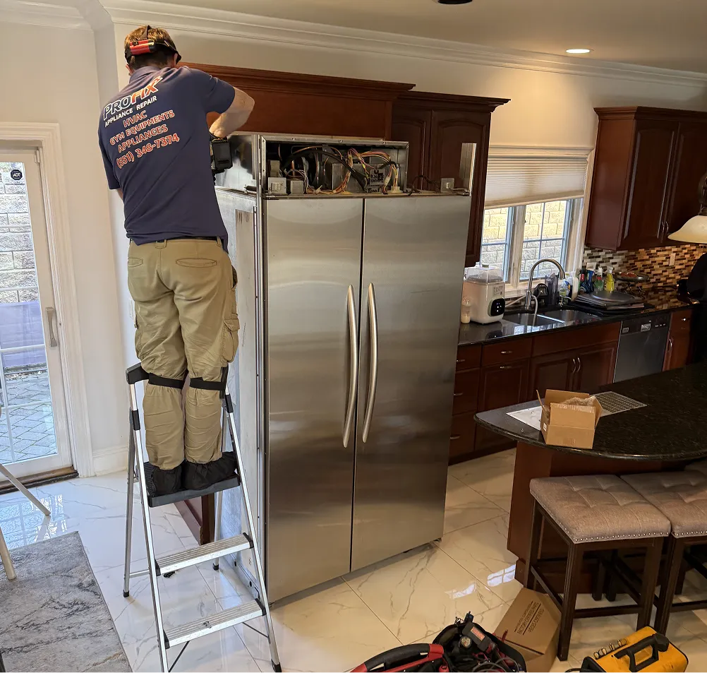 ProFix technician repairing a built-in refrigerator compressor compartment on a ladder in a Bridgewater NJ home