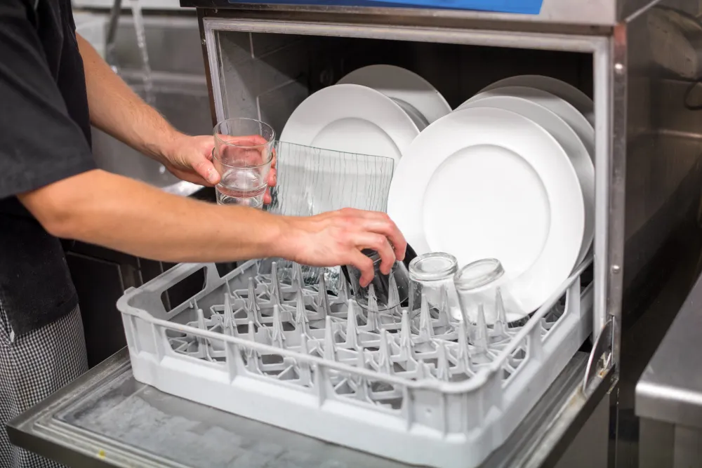 Restaurant staff loading plates and glassware into a commercial dishwasher