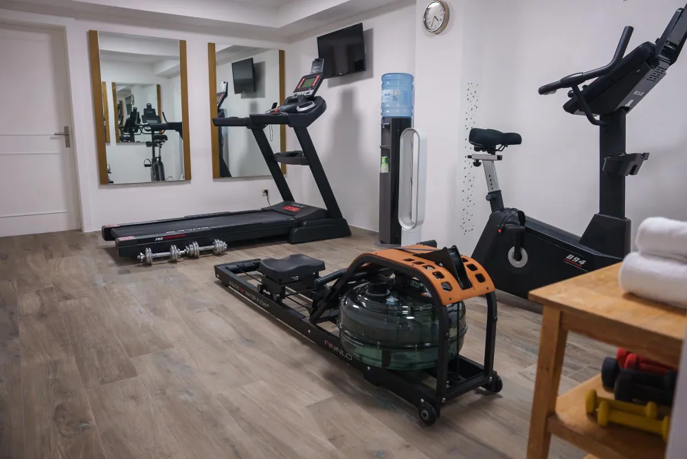 A small gym with a rowing machine, treadmill, stationary bike, and dumbbells on a wood floor.