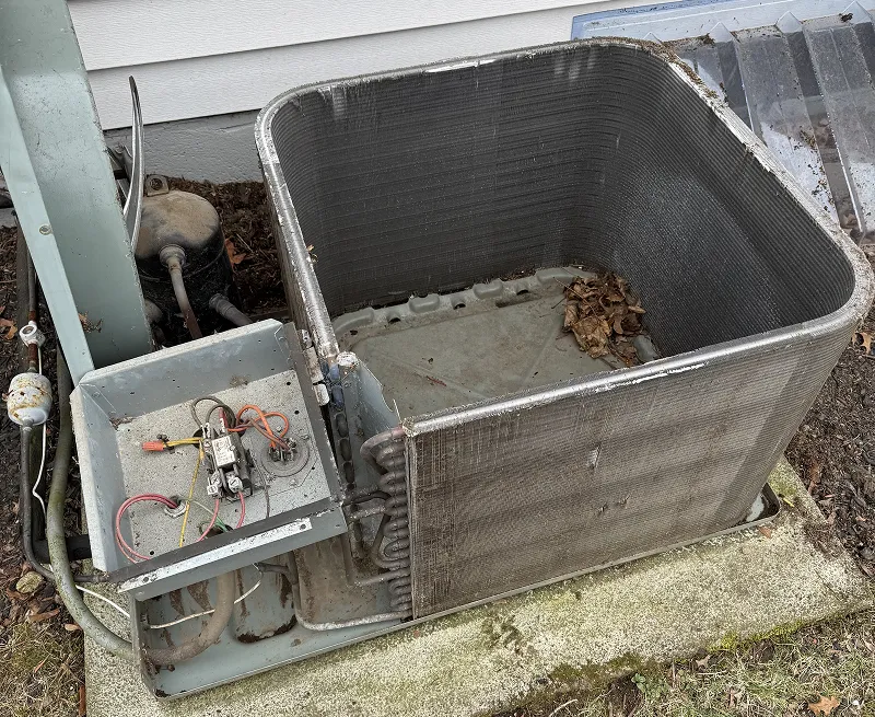 An open, weathered outdoor AC condenser unit with debris inside