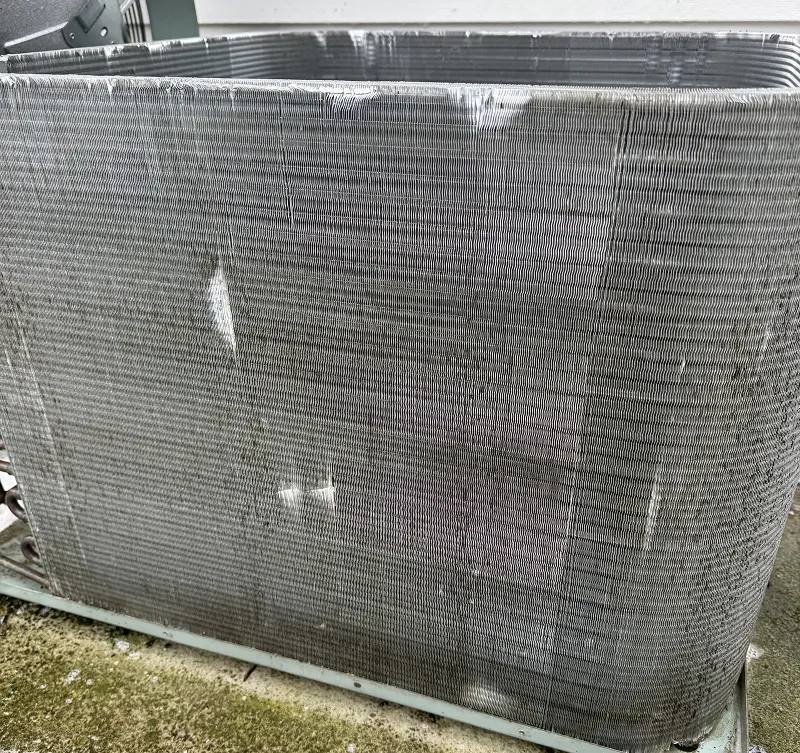 Close-up of a dirty, clogged AC condenser coil with visible damage and bent fins.