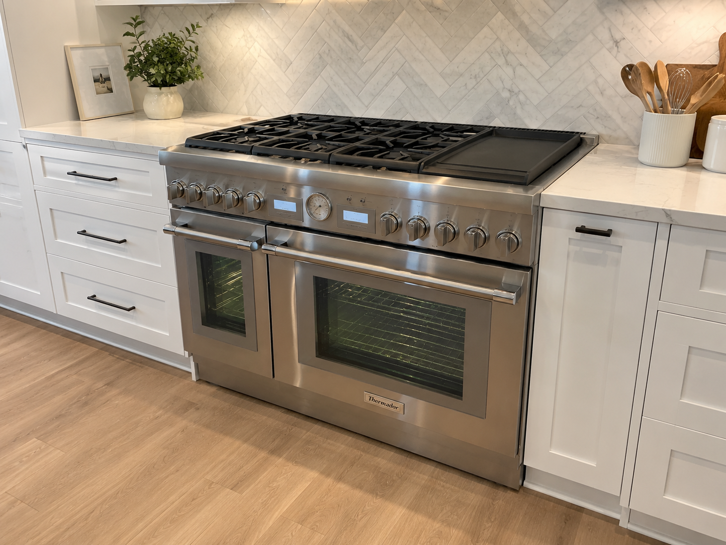 Stainless steel Thermador refrigerator and range in a modern white kitchen with wood flooring