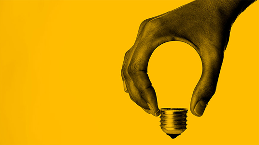 Hand holding a light bulb against a yellow background.