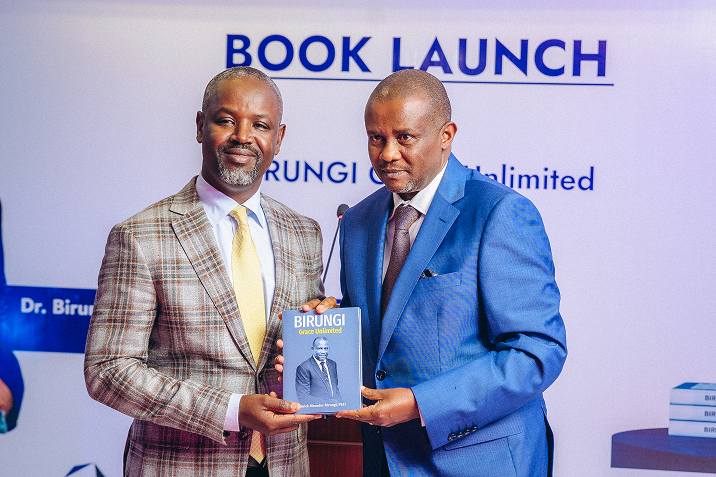 Two men in suits holding and presenting a book titled 'Birungi Grace Unlimited' at a book launch event.