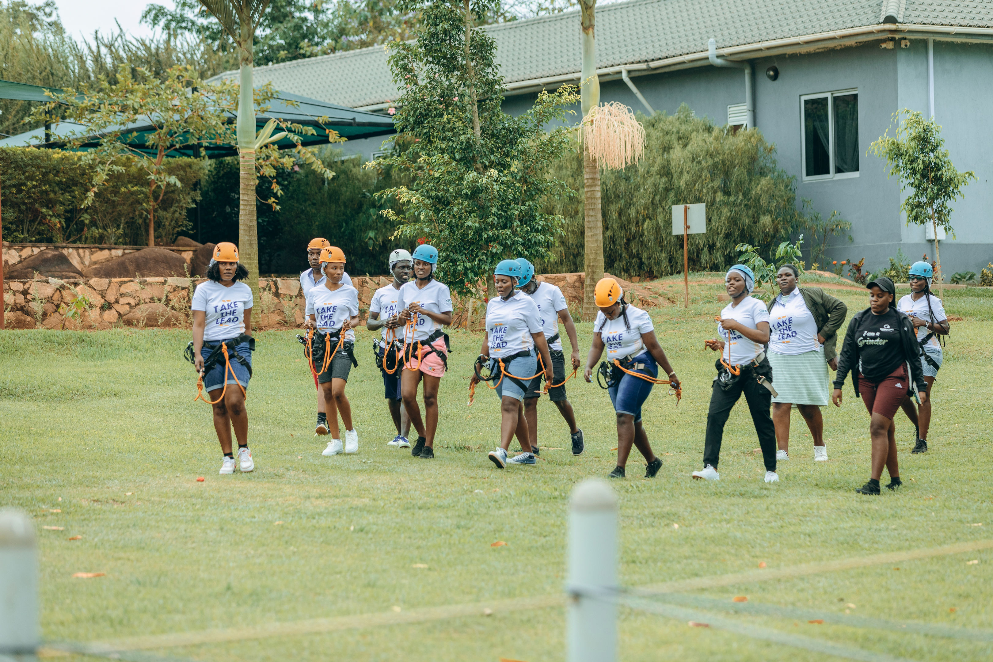 Group of people wearing helmets and harnesses walking on a grassy field during a team-building event.