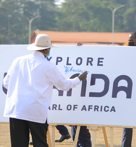 Person wearing a white shirt and hat signing a large board with the text 'EXPLORE UGANDA THE PEARL OF AFRICA.'