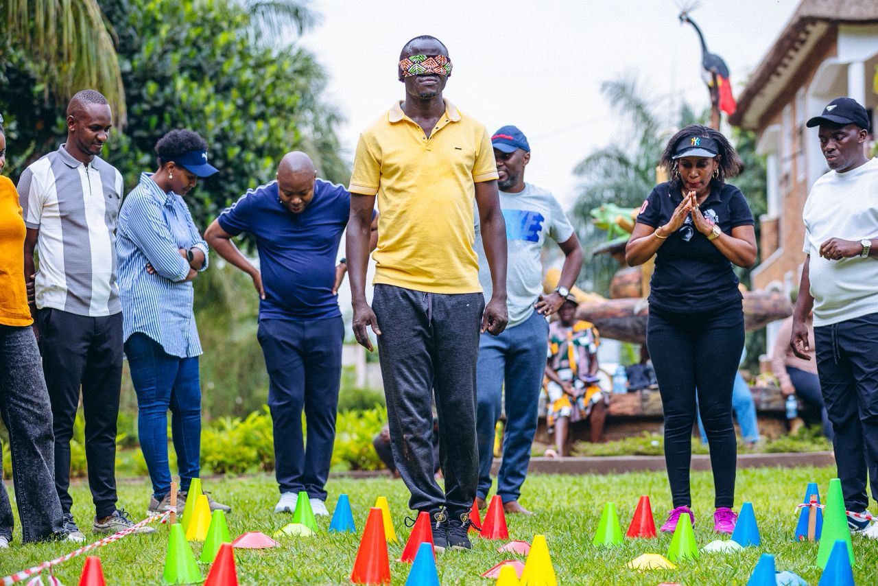Group of adults participating in an outdoor team-building activity with colorful cones, one man blindfolded walking carefully.