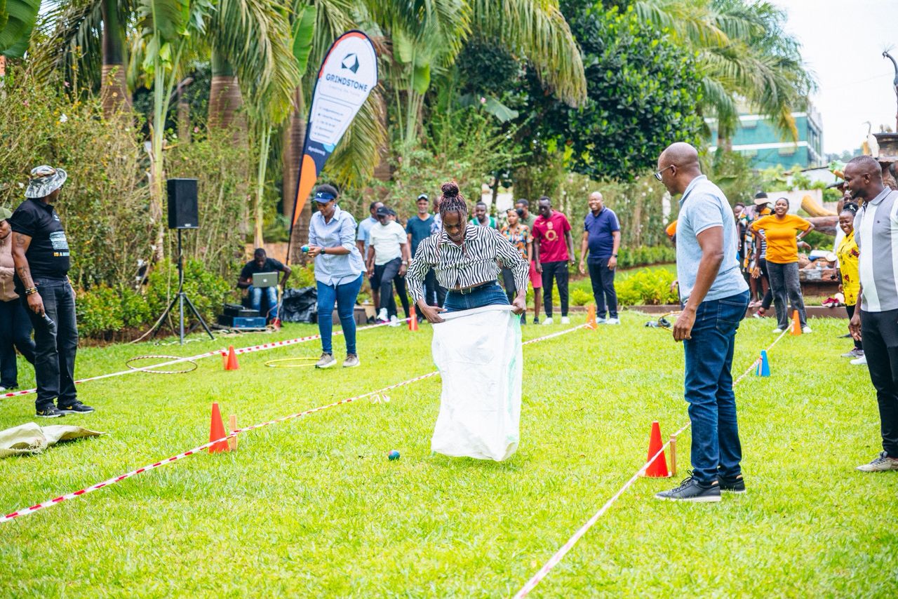 Group of people outdoors participating in a sack race game on a grassy lawn during a team-building event.
