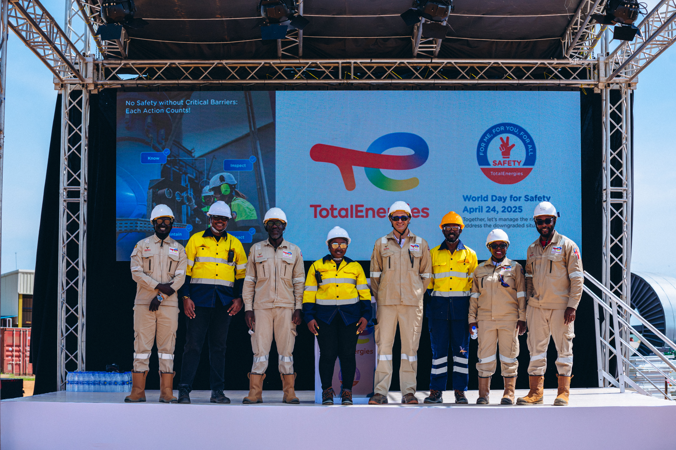 Eight workers in safety gear standing on a stage with TotalEnergies World Day for Safety 2025 signage behind them.