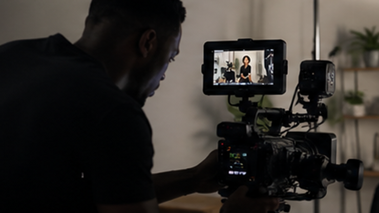 Man operating a professional video camera recording a woman speaking on the camera's screen.