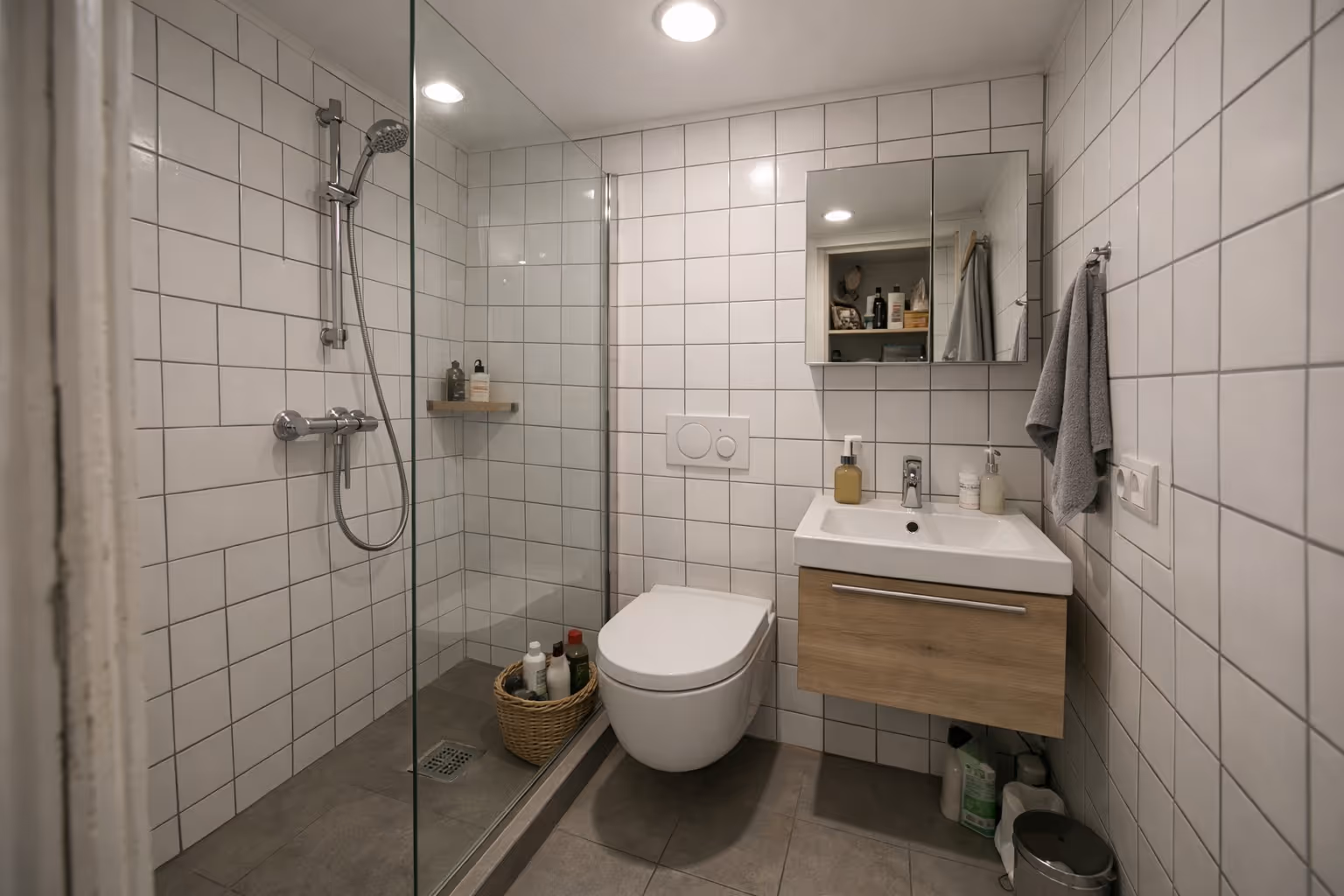Kompaktes modernes Badezimmer mit begehbarer Dusche, weiß gekachelten Wänden, wandhängendem WC und Holzwaschbeckenunterschrank.