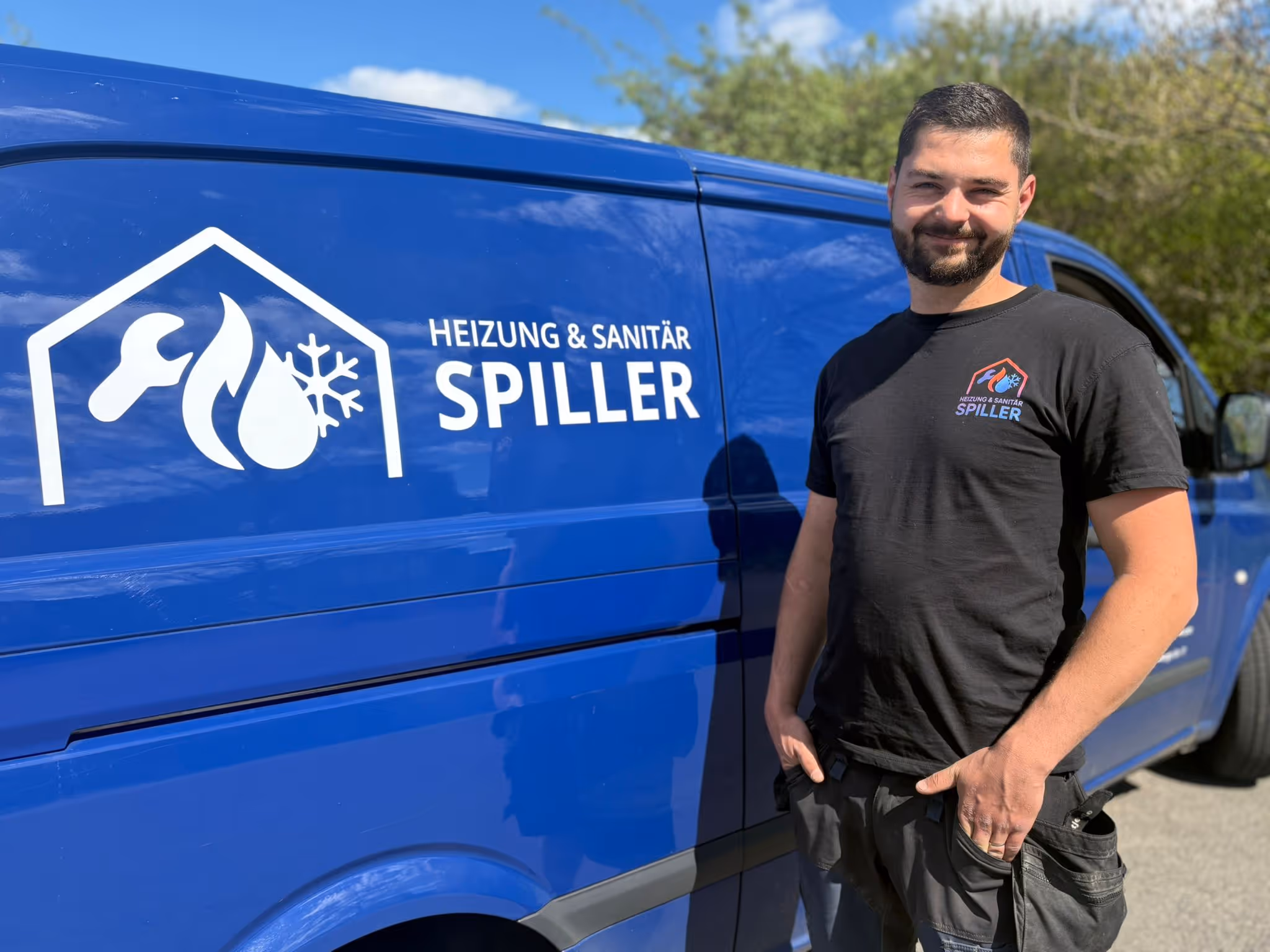 Mann mit schwarzem T-Shirt vor blauem Transporter mit Aufschrift Heizung & Sanitär Spiller.