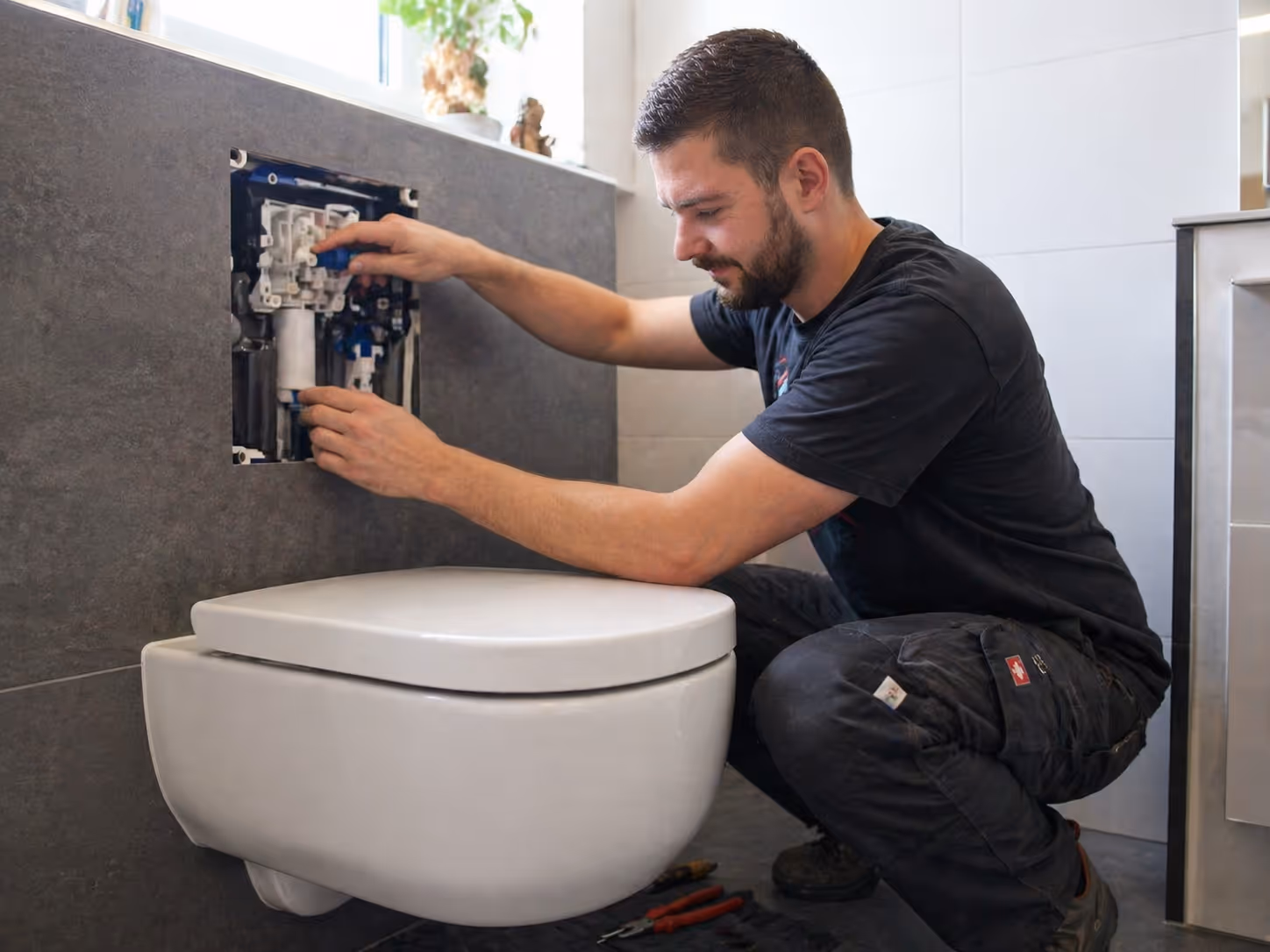 Mann repariert die innere Mechanik einer Wandtoilette in einem modernen Badezimmer.