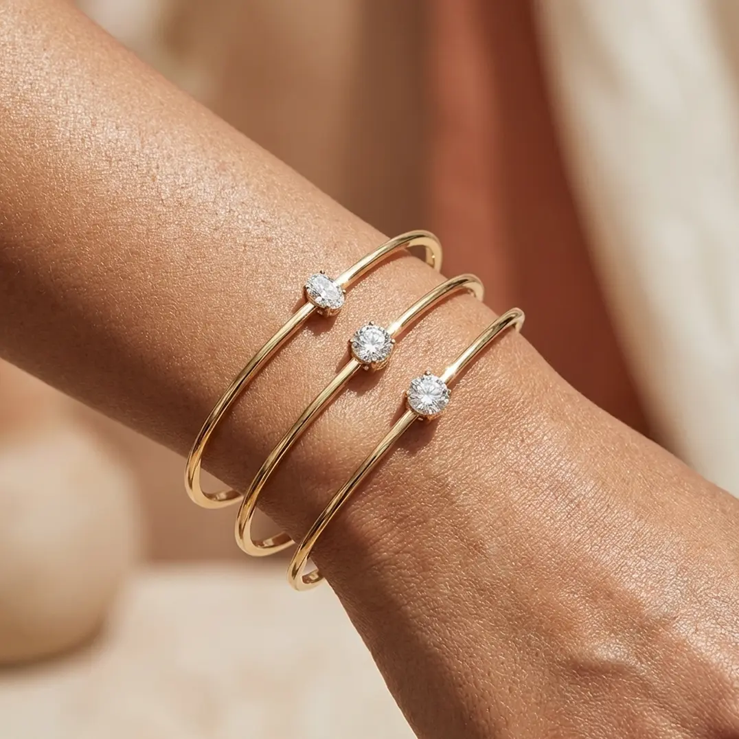 Close-up of a wrist wearing three thin gold bangles, each adorned with a single sparkling diamond.