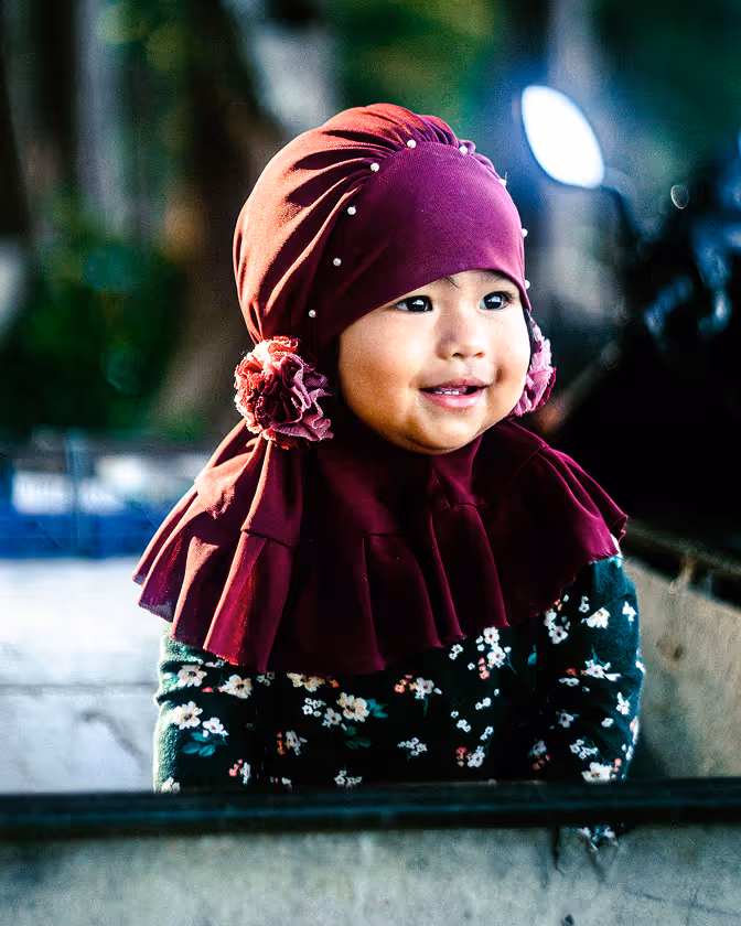 ילדה מחייכת עם צעיף סגול מעוטר בפרחים ופנינים, ולבושה בסוודר כהה עם דוגמת פרחים.