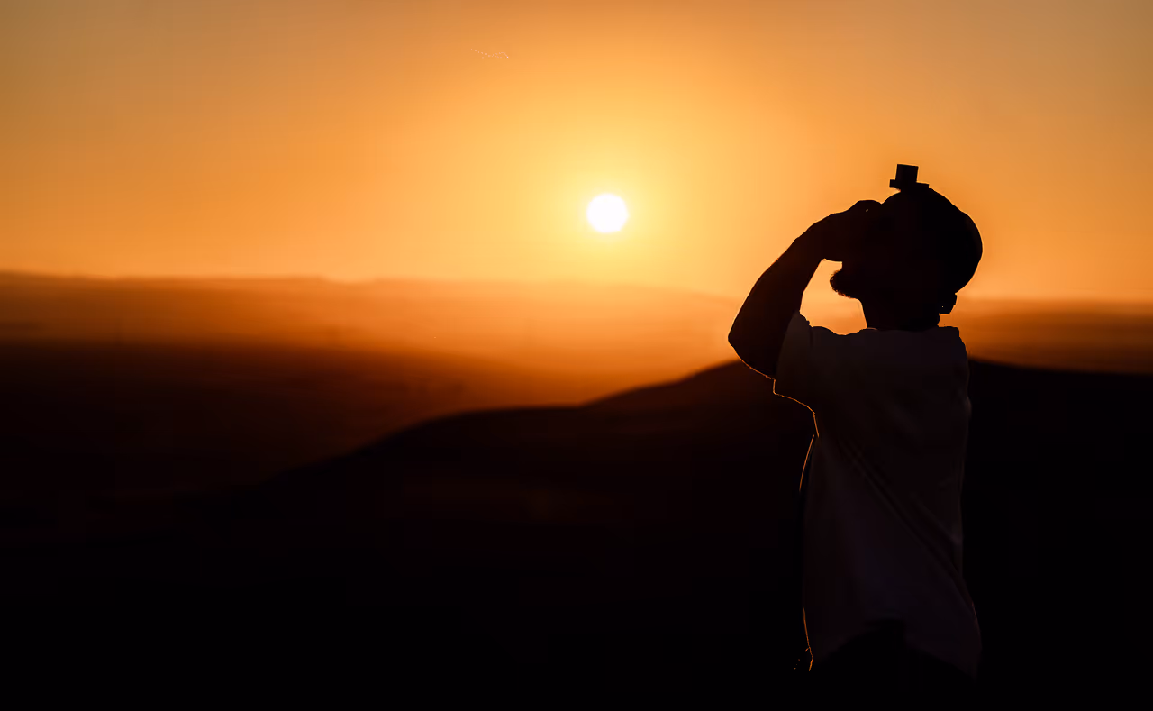 צללית של אדם עם כיפה וחפות מזוזה על ראשו בשקיעה במדבר.