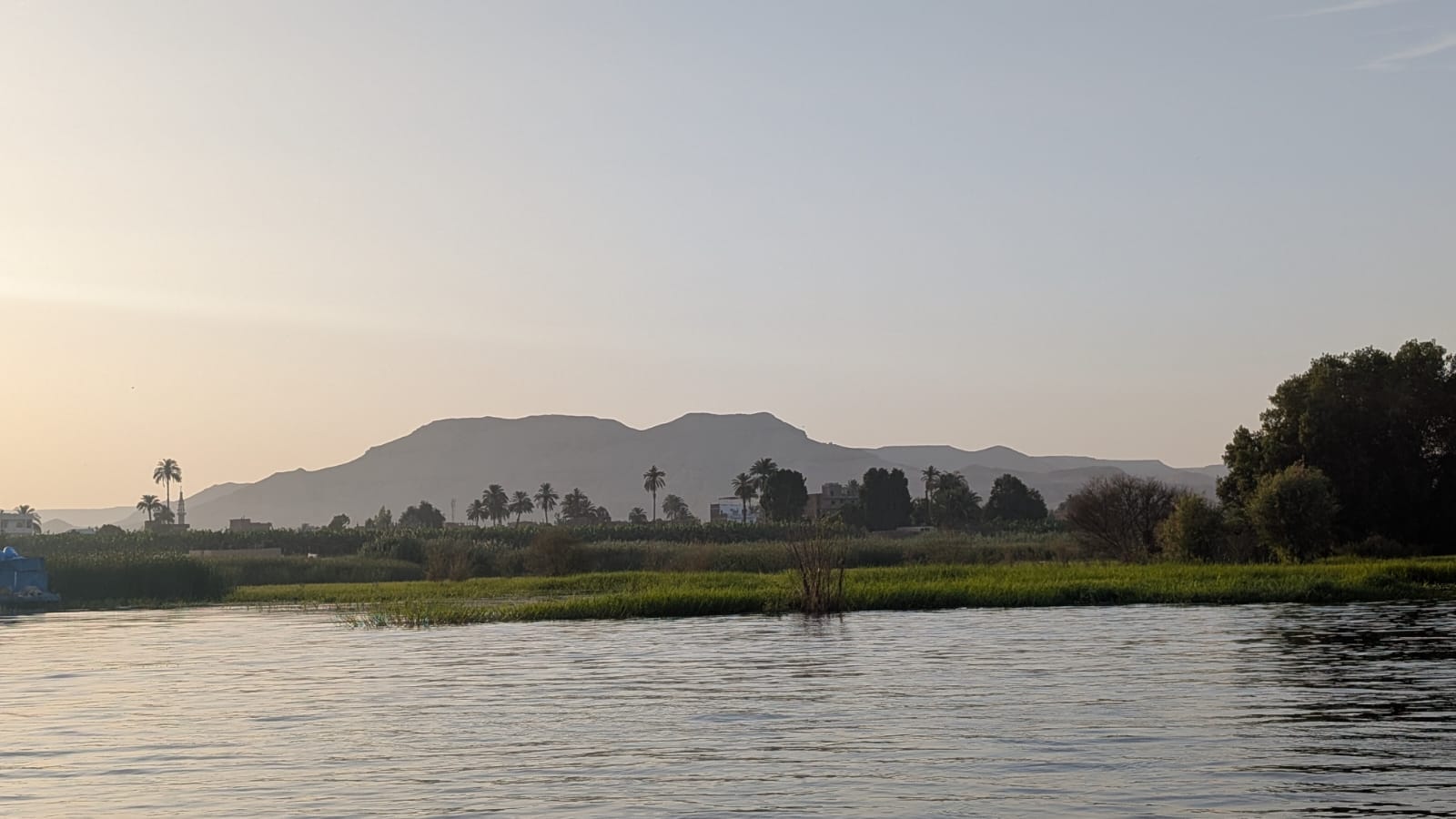 View across the Nile toward Luxor's West Bank — open farmland, wide sky, and the Theban Mountain in the distance