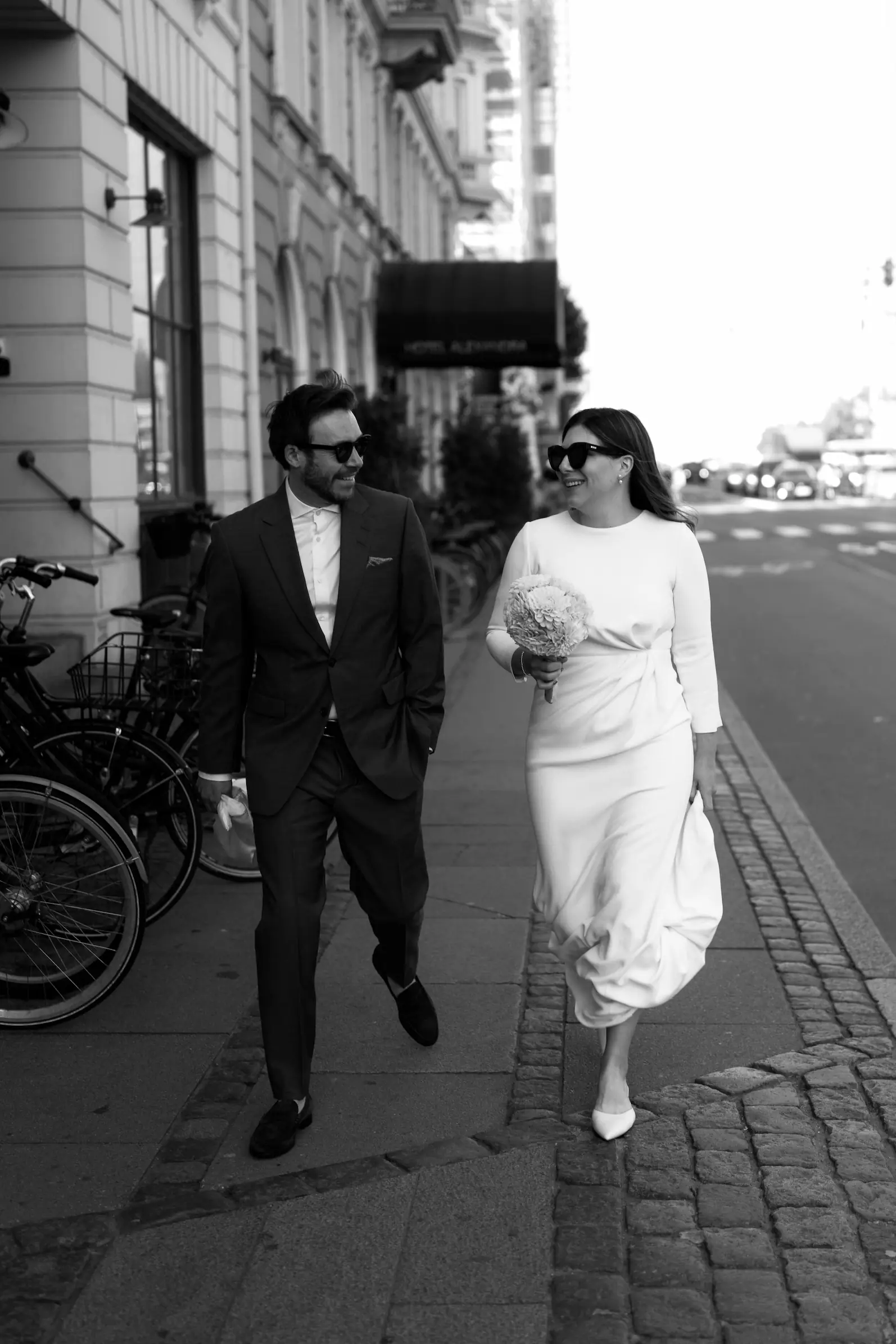 Bride and groom holding hands, walking along a street.