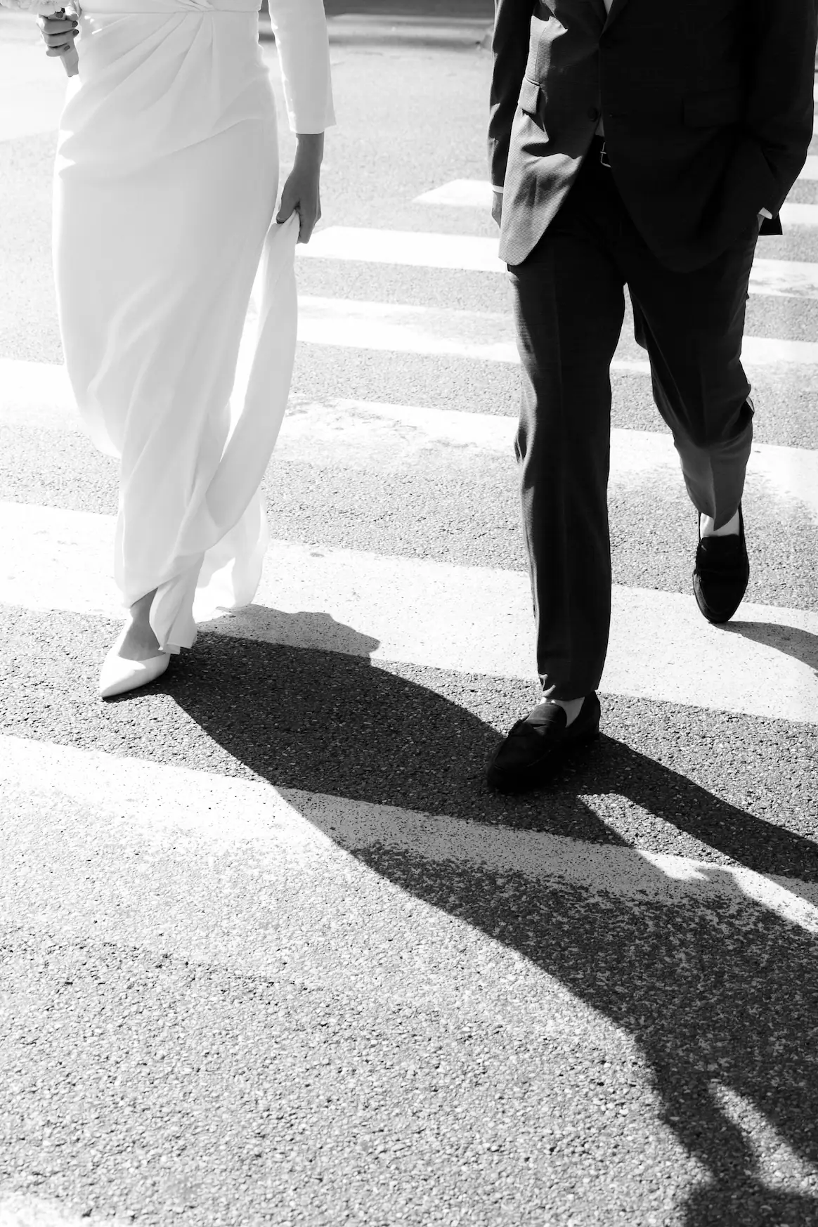 Black and white image of a couple walking down a street - detail of legs.