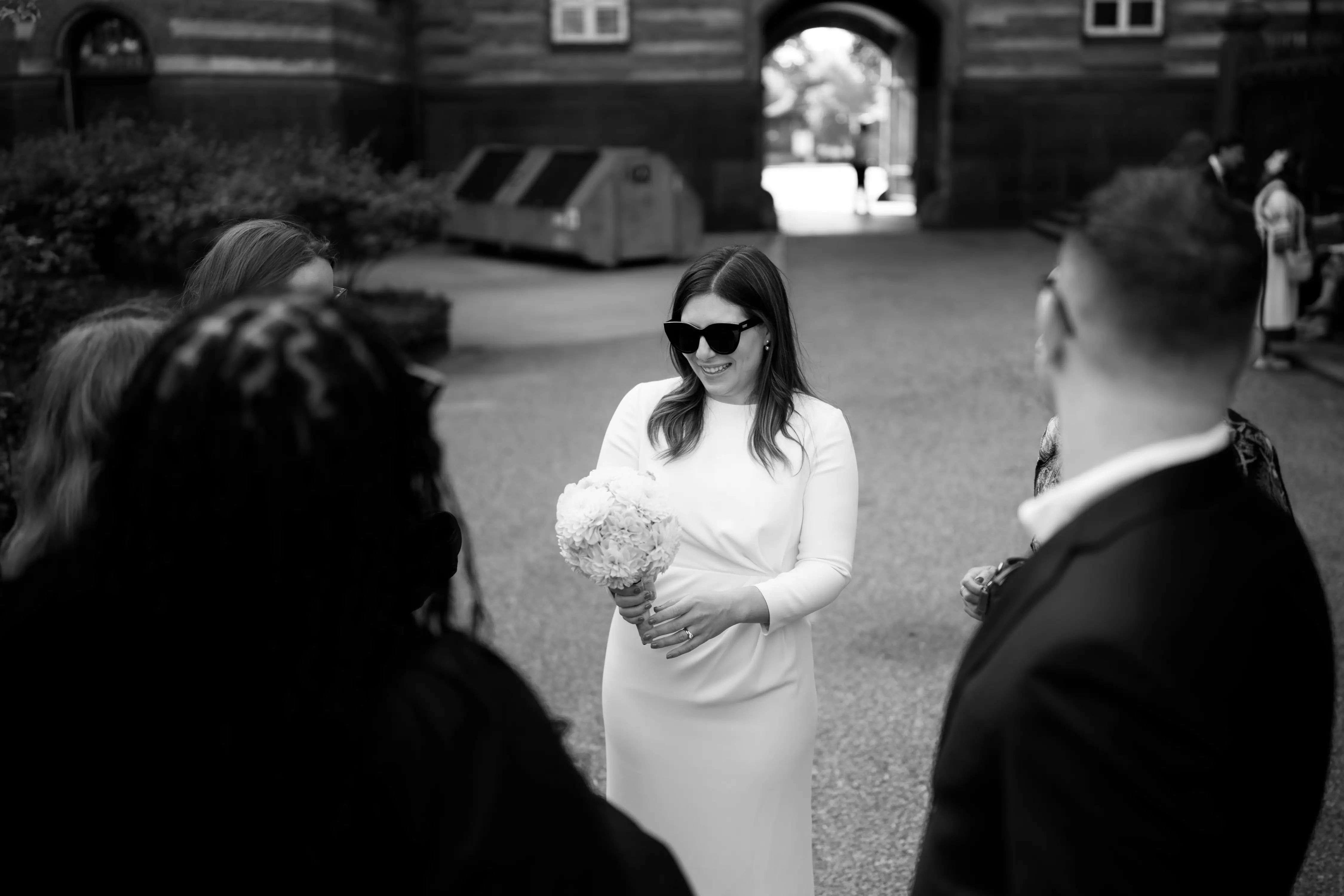 A bride with a boquet and sunglasses talking to people