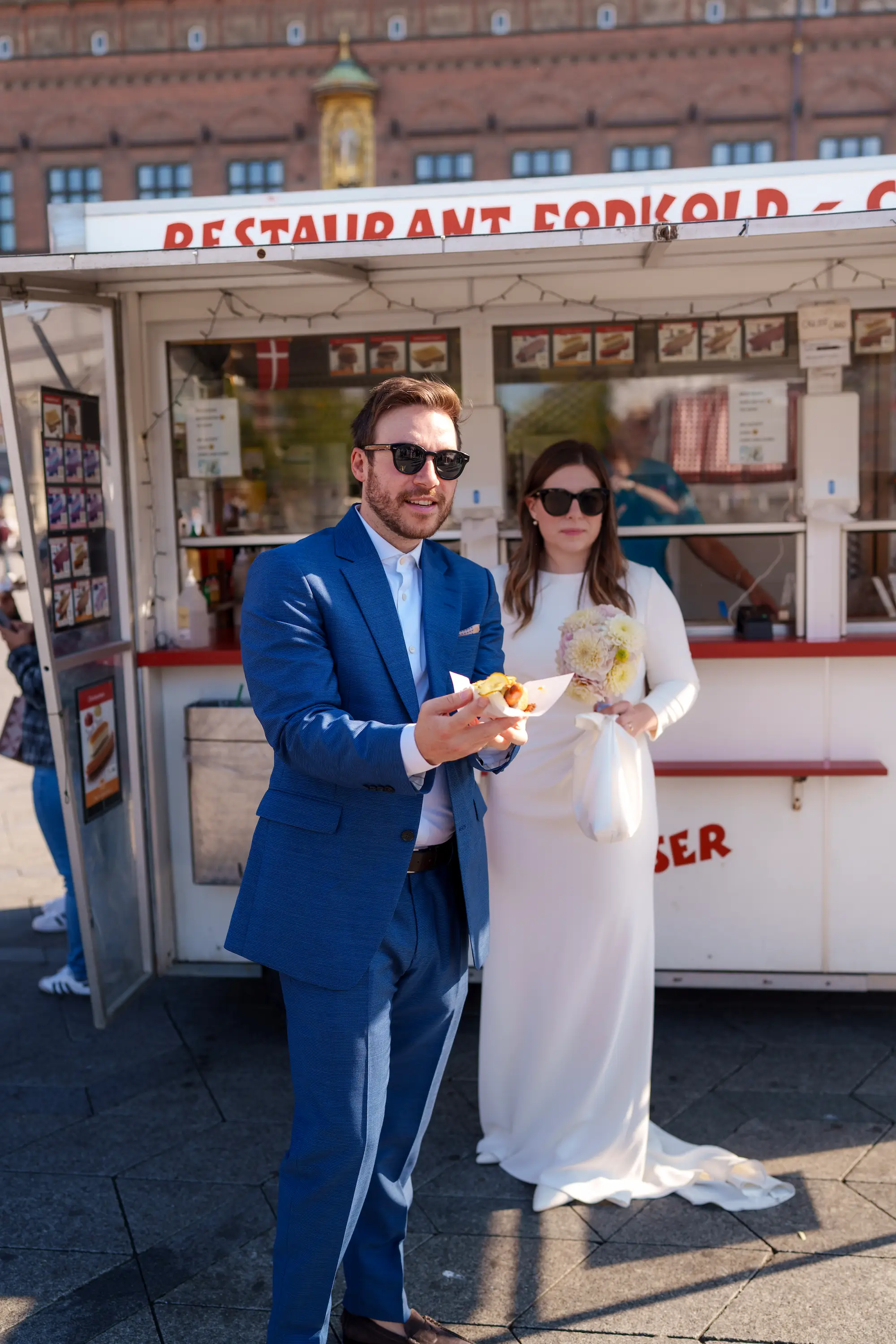 A bride and groom buying a hot dog at a stand while in formal dress