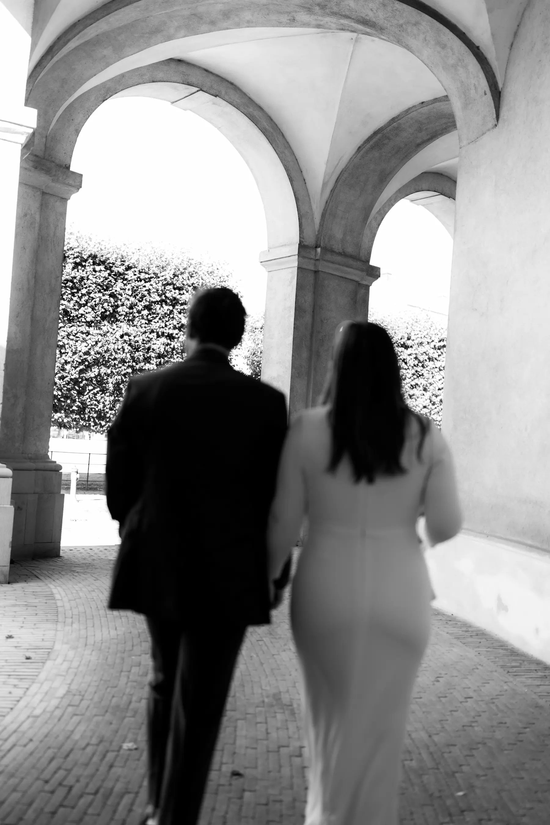 Blurry black and white image of a bride and groom walking in a courtyard