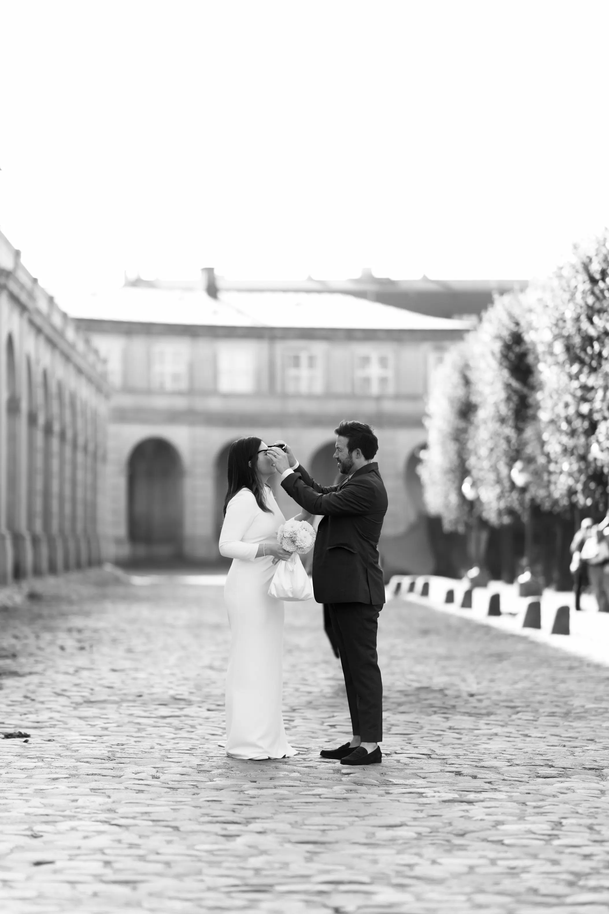 Groom placing sunglasses on the bride in an open courtyard