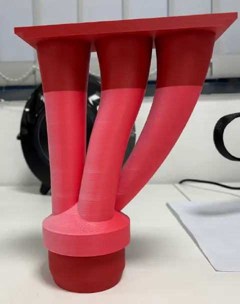 Un objet rouge imprimé en 3D avec trois tubes incurvés convergeant vers une base circulaire plate.