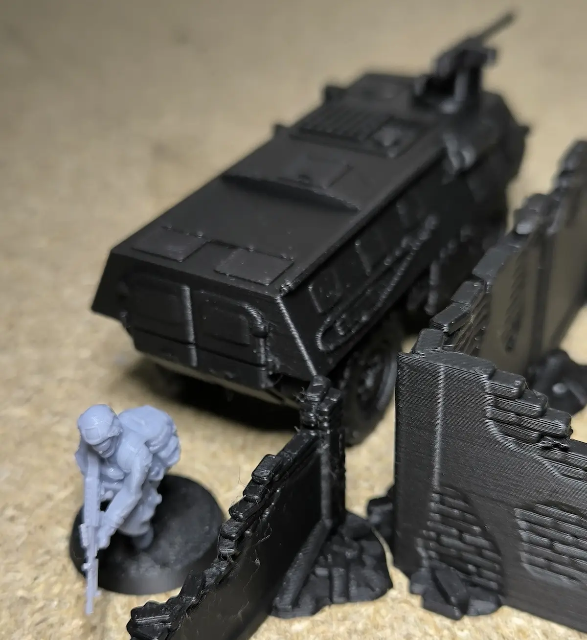 Figurine de soldat gris avec fusil à côté d'un véhicule blindé noir et un mur de ruines en plastique noir.