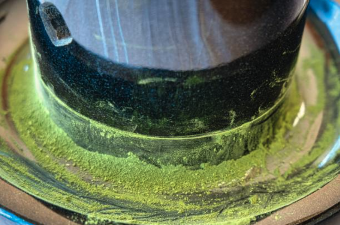 Granite stone mill grinding tencha into matcha, with fresh green powder collecting around the base.