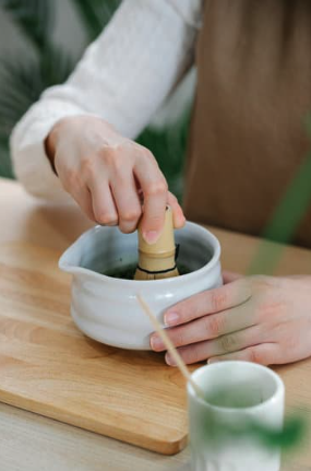 Barista whisking matcha in a spouted ceramic bowl with a bamboo whisk.