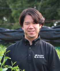 Shinichiro Arai standing in the tea field in a black Arai-en polo shirt