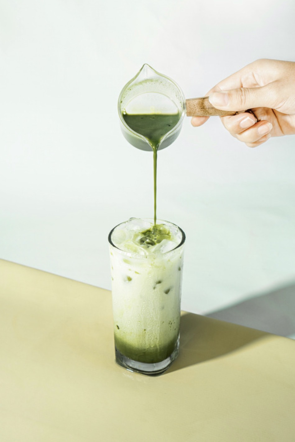 Matcha concentrate poured from a glass pitcher into an iced latte.