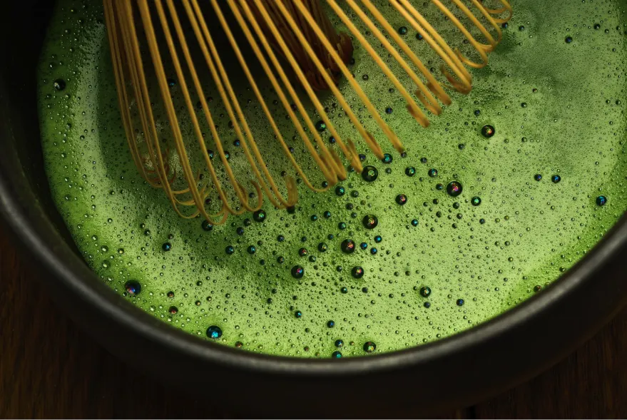 Close-up of freshly whisked ceremonial grade matcha with a fine foam, bamboo whisk resting in the bowl.