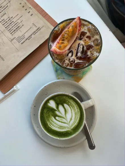 Hot matcha latte with rosetta latte art beside an iced drink and a cafe menu on a white table.