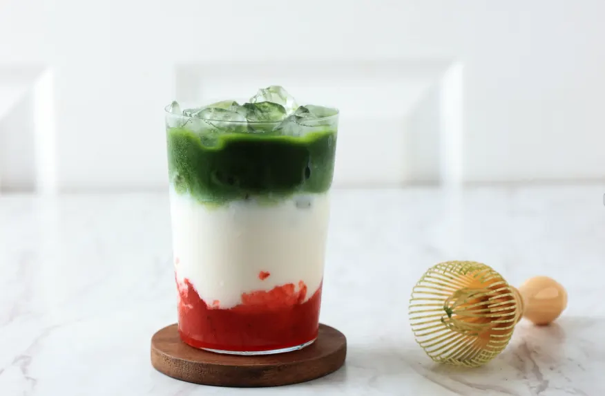 Layered iced strawberry matcha latte with a red strawberry base, white milk middle, and green matcha top.