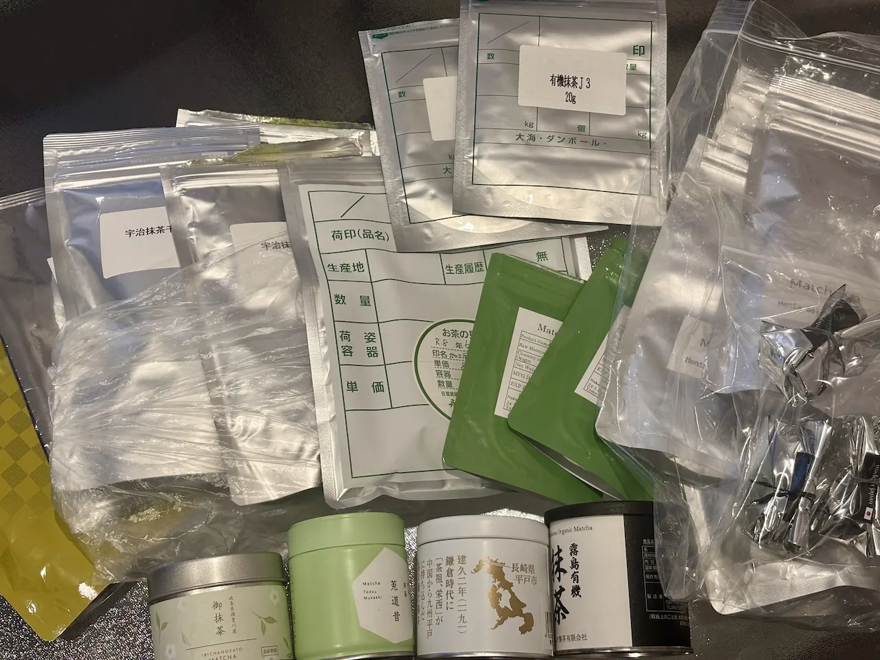 Matcha samples laid out for evaluation: labelled sample bags, a Japanese product spec sheet, and matcha tins.