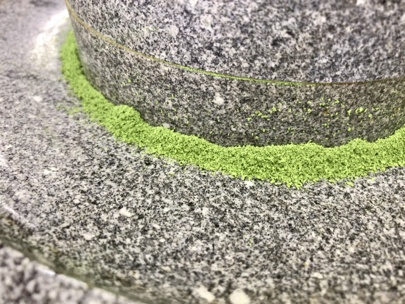 A granite stone mill grinding tencha into a ring of fine bright green matcha powder