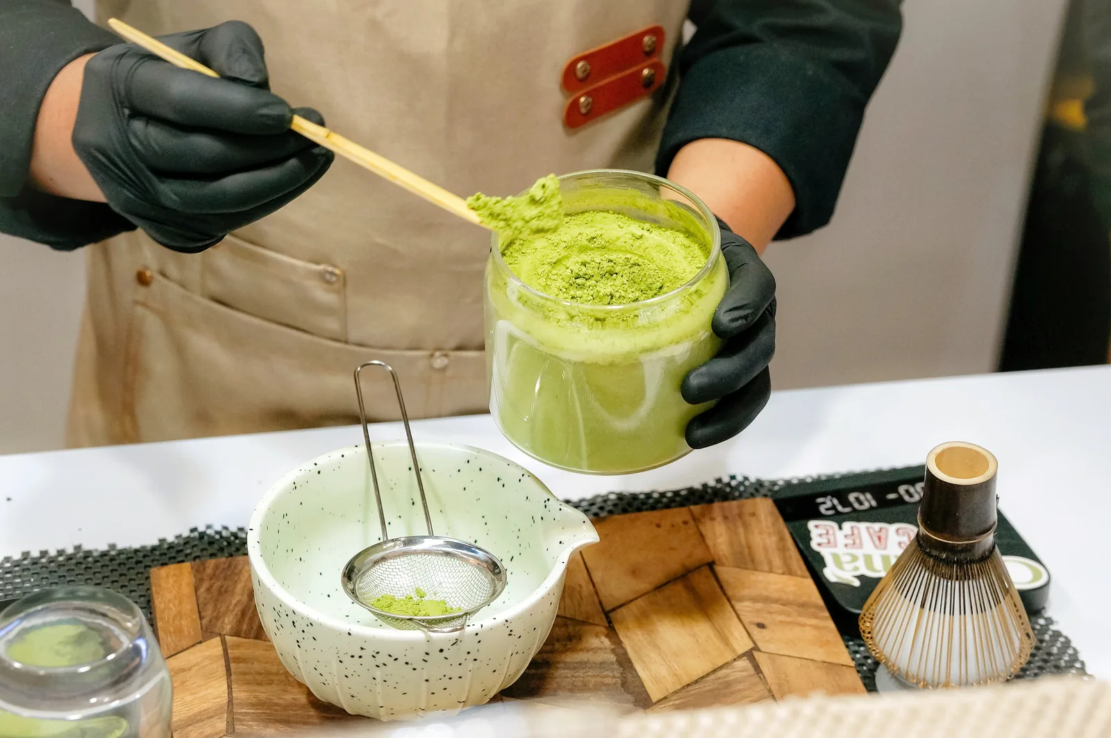 Close-up of gloved hands preparing a matcha drink with a sieve.