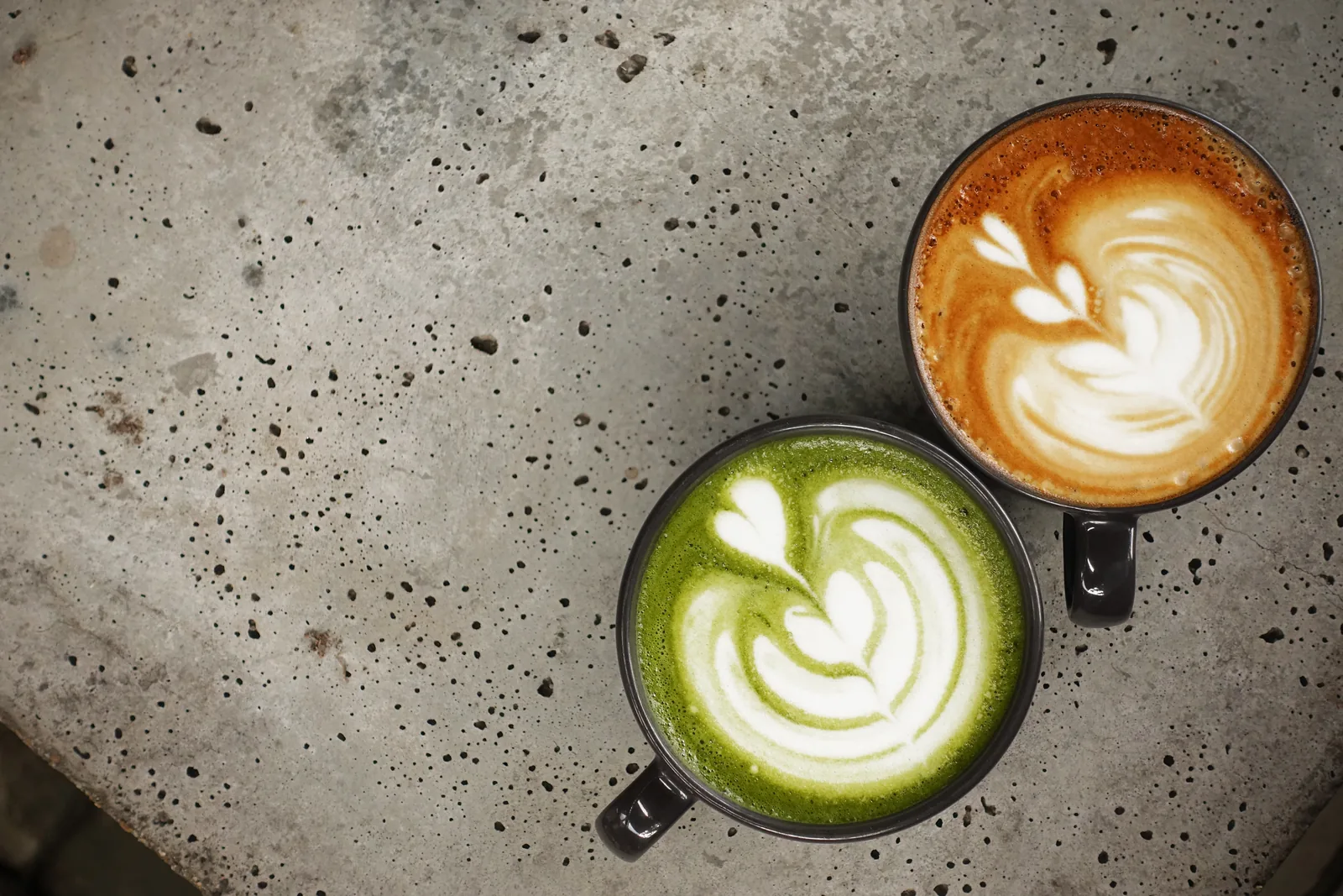 A cup of matcha latte beside a cup of latte art coffee.