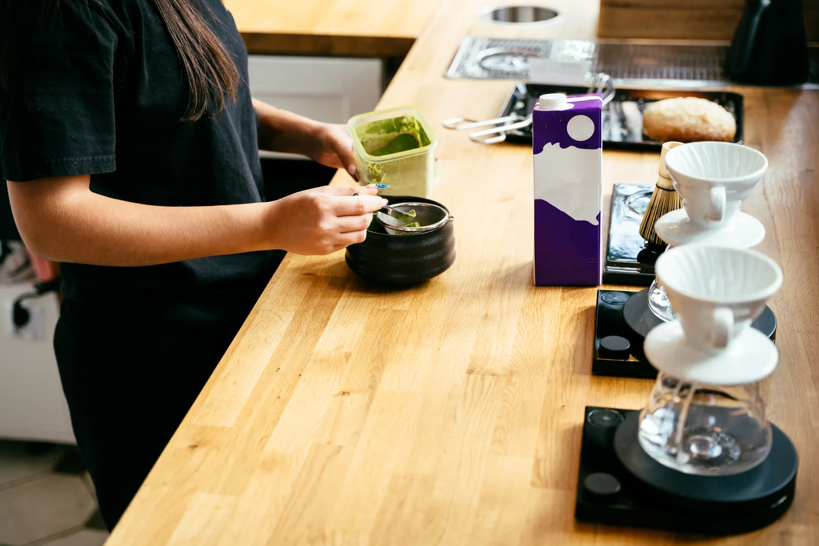 A barista preparing a matcha drink with traditional tools at a specialty coffee shop.