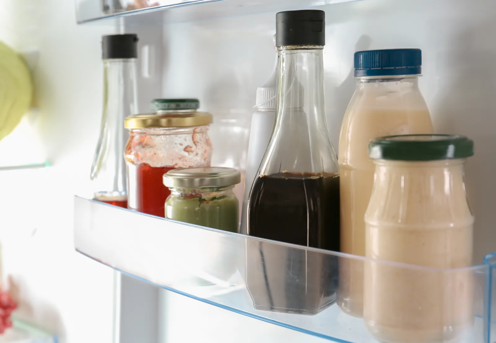 Bottles and containers lined up on a refrigerator shelf.