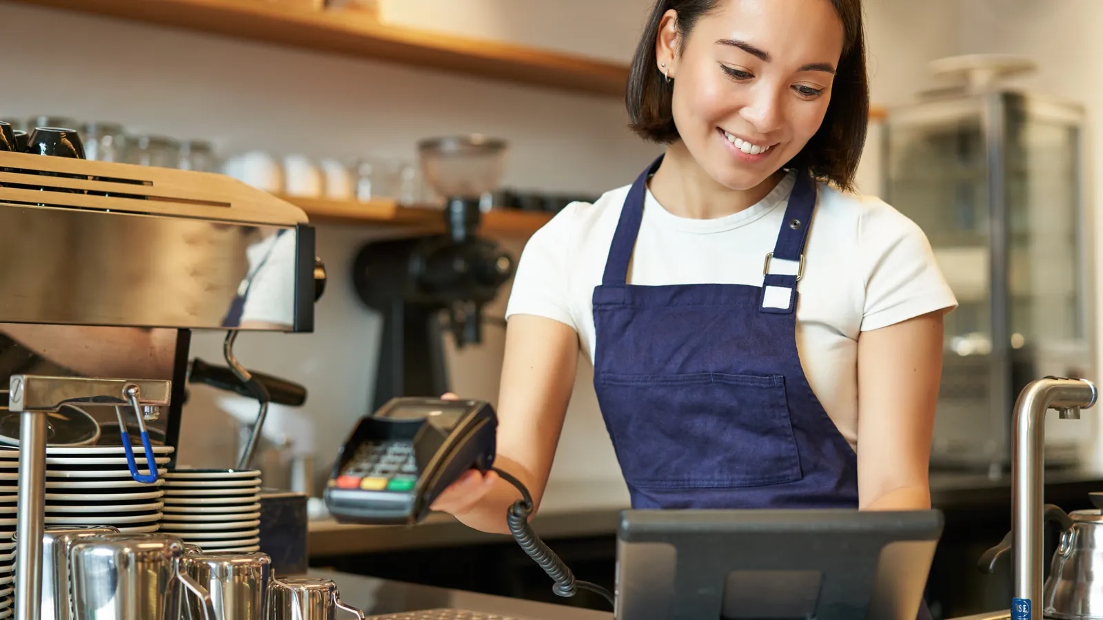 A barista taking an order at the point of sale terminal behind a cafe counter.