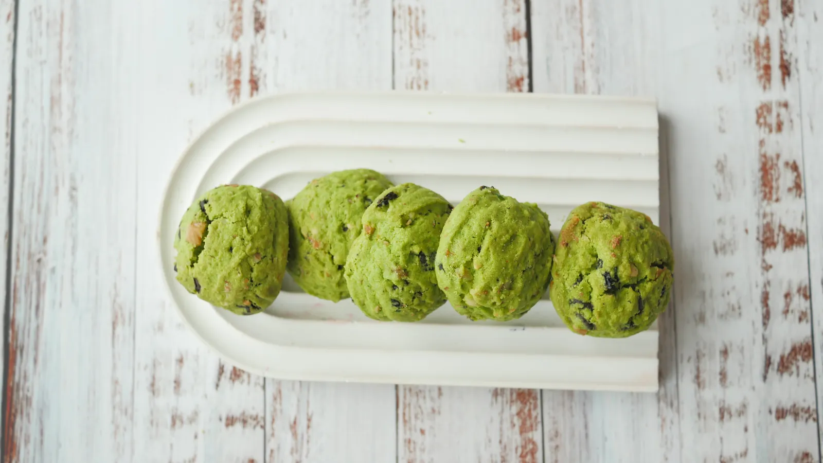 A row of baked matcha cookies on a white ceramic tray.