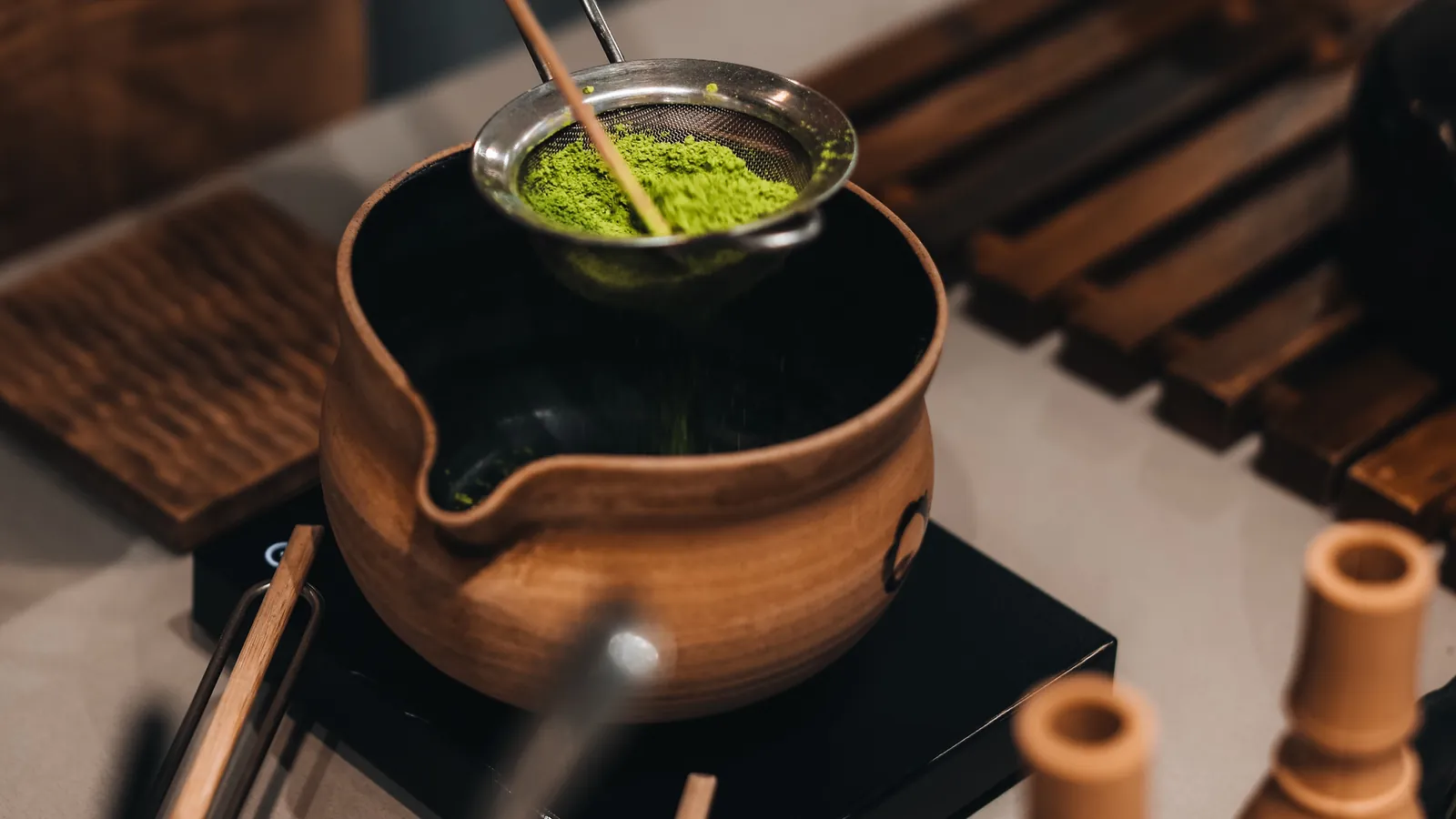 A copper kettle, a fine strainer holding matcha powder, and a set of tea tools on a counter.